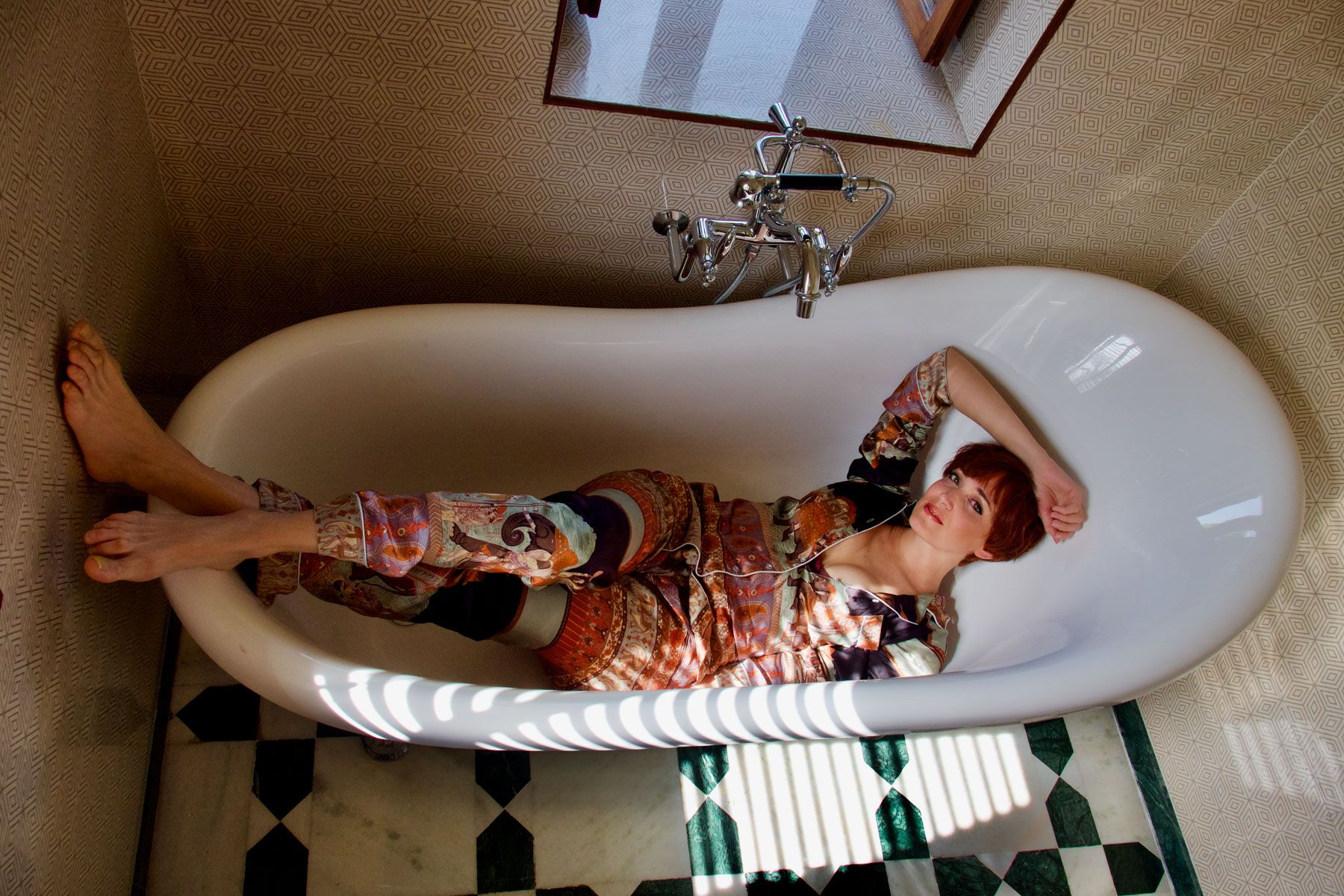 Woman lying in a white clawfoot bathtub on a checkerboard floor