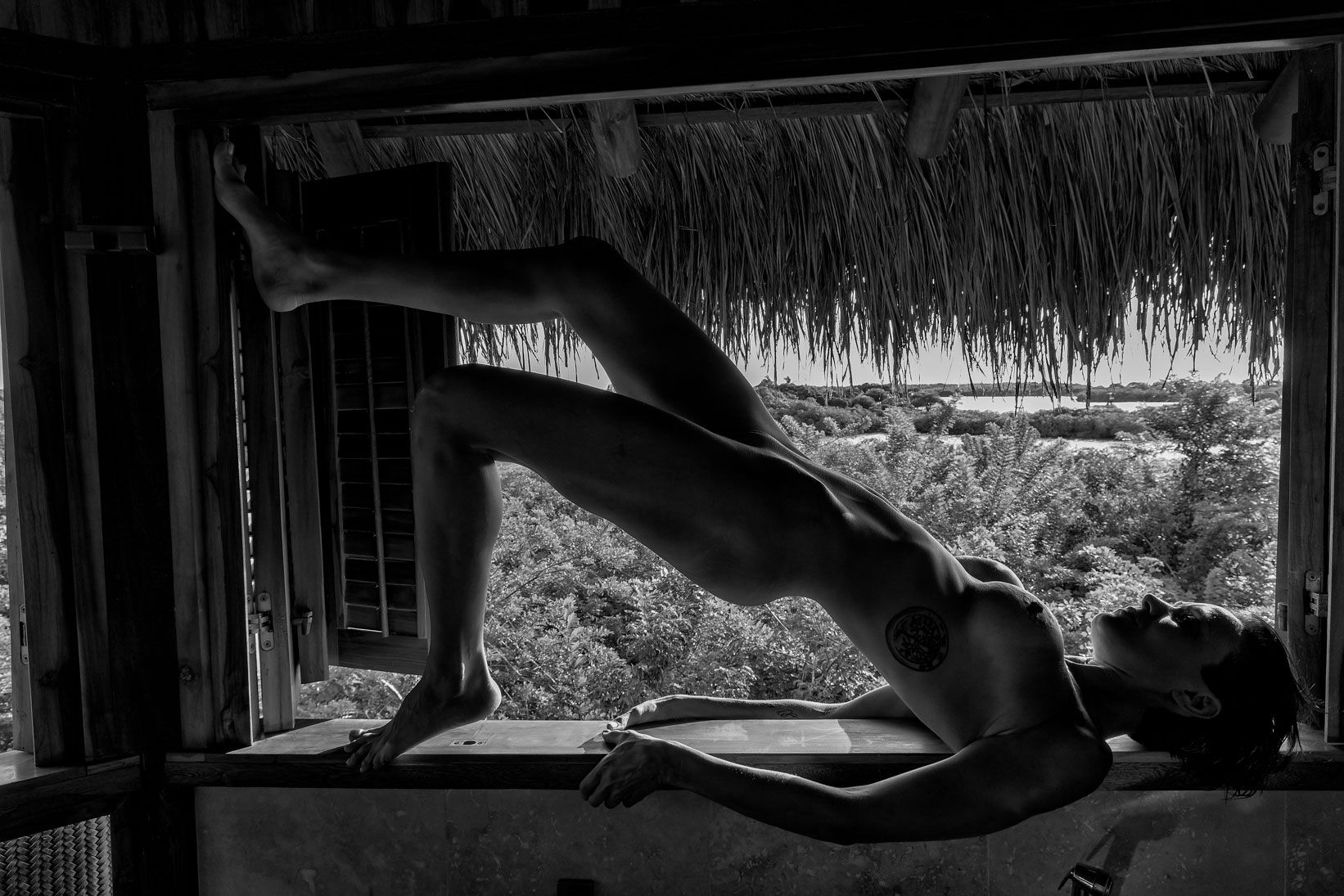 Black and white photograph of a woman lying in an open window above a garden